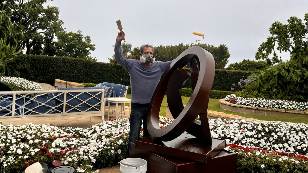 Sculptor John Branstetter finishing a large bronze abstract sculpture outdoors in a garden setting.
