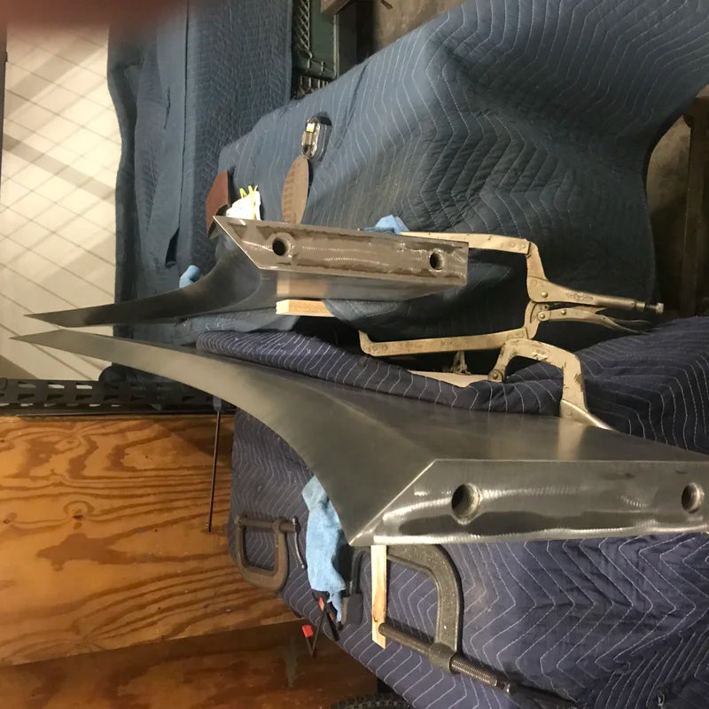 Curved stainless steel fabrication pieces resting on protective moving blankets in a workshop, part of a custom metal fabrication project.