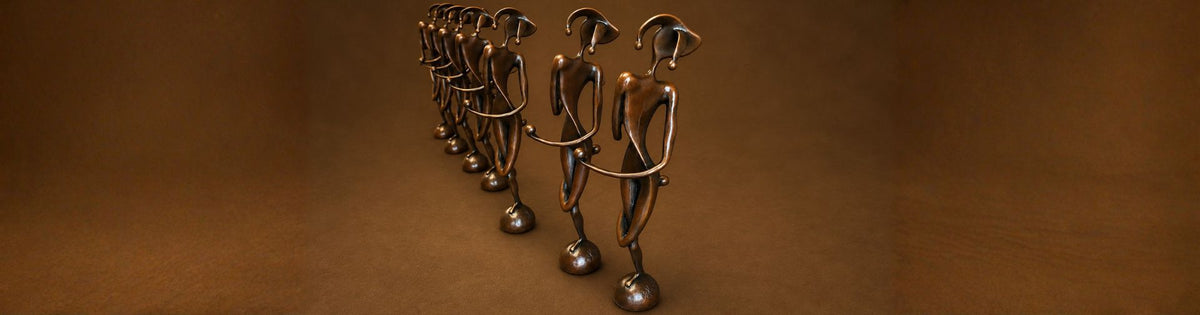 A row of metallic bronze figurative sculptures standing in a line against a warm brown gradient background.