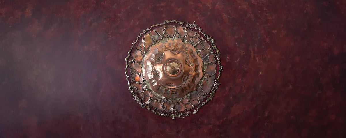 A round, distressed bronze metal emblem or medallion with a decorative, textured border, centered on a dark reddish-brown textured background.